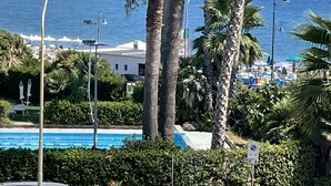 A pool area with palm trees, a building, and a view of the ocean.