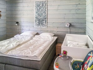 A bedroom with a bed, a crib, a wall-mounted light, and a decorative wall piece. - Villa blombacka by Interhome (Loviisa)