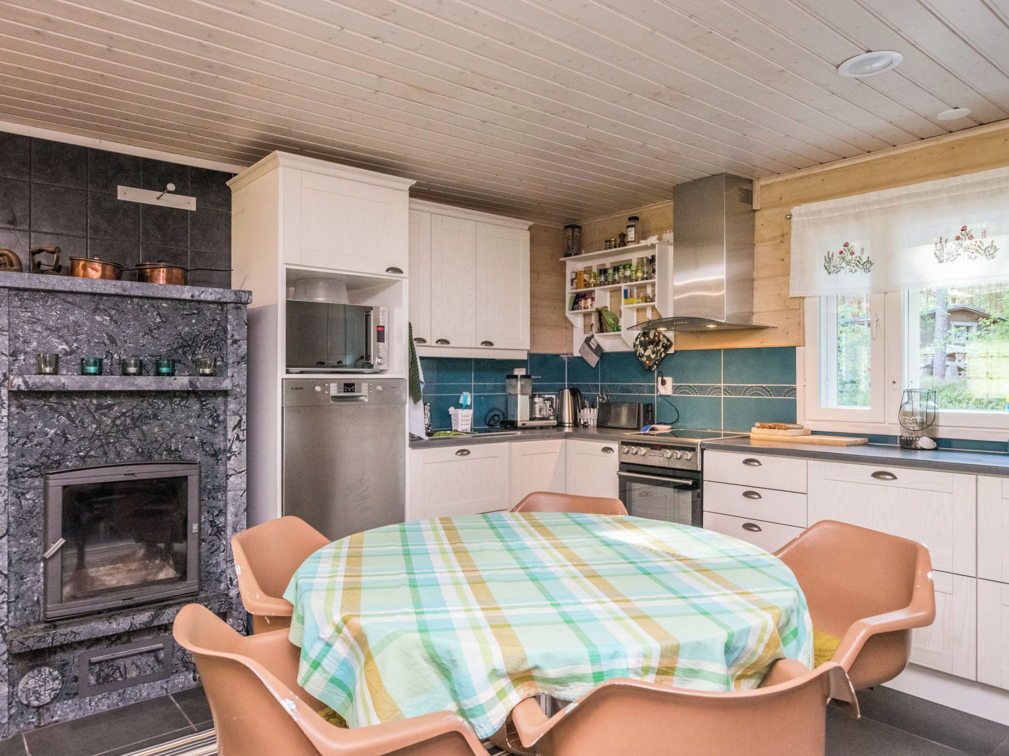 Una cocina con chimenea de piedra, electrodomésticos modernos y un comedor con mantel escocés.
