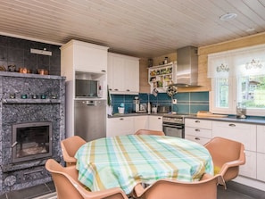 A kitchen with a stone fireplace, modern appliances, and a dining area with a plaid tablecloth. - Villa blombacka by Interhome (Loviisa)