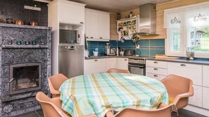 Een keuken met een open haard, moderne apparatuur en een eethoek met een geruit tafelkleed.