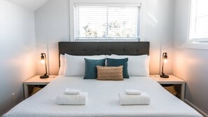 A neatly made bed with white linens, two pillows, and two bedside lamps. - 5-Minute Walk to Beach & Boardwalk, Full kitchen! (Carolina Beach)