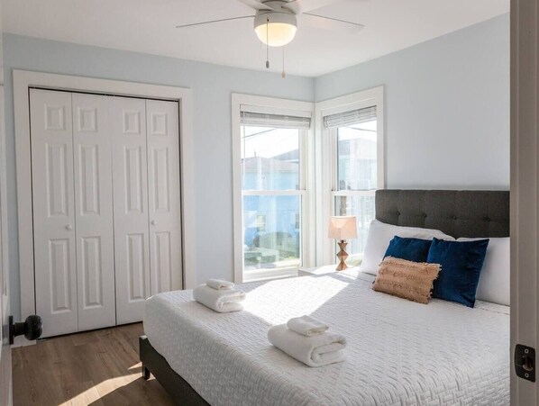 Ein Schlafzimmer mit Bett, weißen Wänden, Deckenventilator und Ausblick nach draußen.
