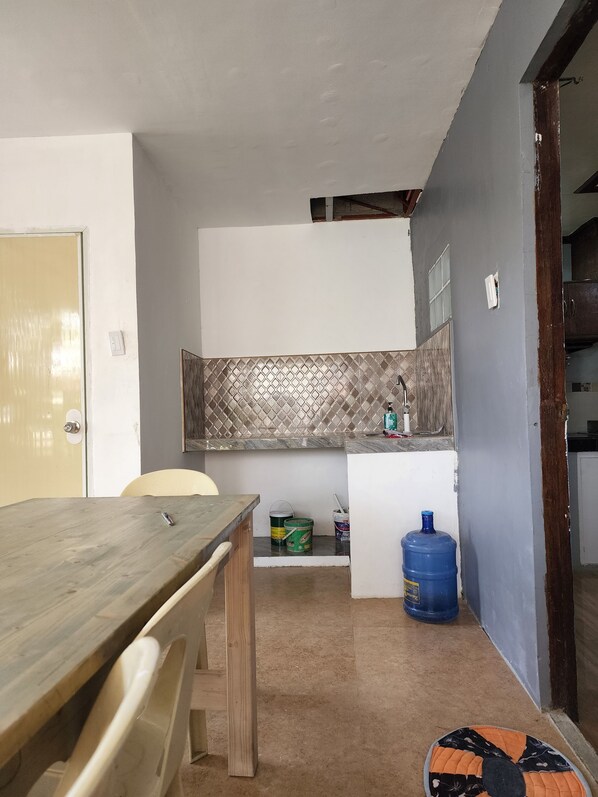 A compact kitchen with a wooden table, chairs, a tiled backsplash, and a blue water dispenser.