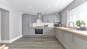 A modern kitchen with grey cabinets, a stainless steel range hood, a built-in oven, and a wooden countertop. - Host & Stay | Sea Breeze (Amble)