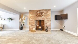 A living room with a brick fireplace, a flat-screen TV mounted on the wall, and a carpeted floor. - Host & Stay | Sea Breeze (Amble)