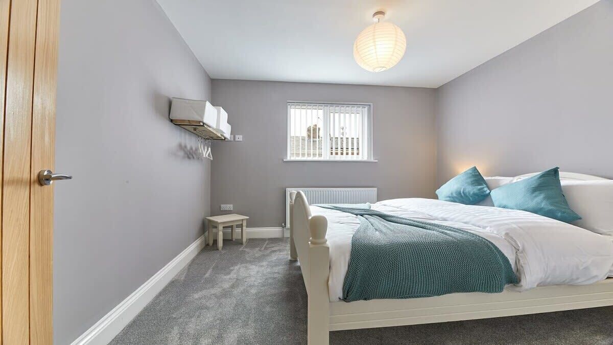 A bedroom with a bed, a small table, a radiator, a window, and a ceiling light.