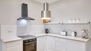 A modern kitchen with white cabinetry, a stainless steel range hood, a built-in oven, a coffee maker, a toaster, and a hanging light fixture. - Host & Stay | Ings Lane (Saltburn-by-the-Sea)