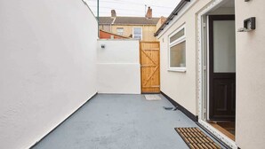 A narrow alleyway with a concrete floor, a wooden gate, and a door leading to a building with a white exterior. - Host & Stay | Ings Lane (Saltburn-by-the-Sea)