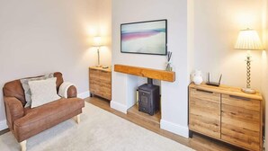 A living room with a brown leather sofa, a wooden cabinet, a fireplace, and two wall-mounted lamps. - Host & Stay | Ings Lane (Saltburn-by-the-Sea)