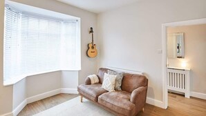 A room with a brown leather sofa, a guitar, a window with blinds, and a radiator. - Host & Stay | Ings Lane (Saltburn-by-the-Sea)