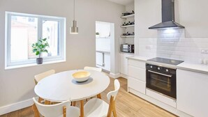 A modern kitchen with a round dining table, white chairs, a black oven, and a window with a plant. - Host & Stay | Ings Lane (Saltburn-by-the-Sea)
