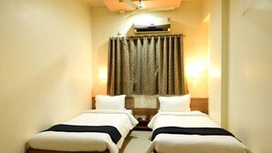 A hotel room with two single beds, a ceiling fan, an air conditioning unit, and a curtain with a leaf pattern. - Hotel Matrix Inn (Rajgurunagar)