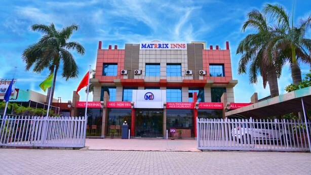 A Matrix Inns hotel with a modern facade, multiple entrances, and a sign indicating a vegetarian and non-vegetarian restaurant. - Hotel Matrix Inn (Rajgurunagar)