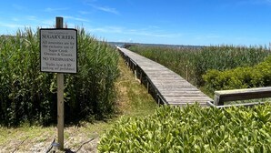 A wooden boardwalk leading through a marshy area with a sign indicating exclusive use for Sugar Creek Owners & Guests. - La Dolce Vita II: Soundfront condo w/sunset views, community pool, 2 en-suites! (Nags Head)