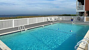 A clear blue pool with white deck chairs and a view of the ocean. - La Dolce Vita II: Soundfront condo w/sunset views, community pool, 2 en-suites! (Nags Head)