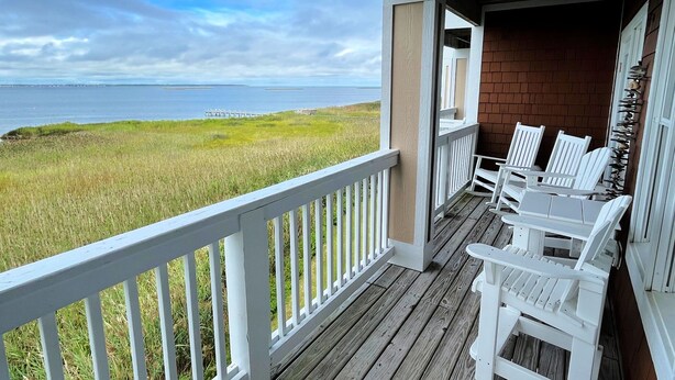 A wooden deck with white railings overlooking a grassy area and the sea. - La Dolce Vita II: Soundfront condo w/sunset views, community pool, 2 en-suites! (Nags Head)