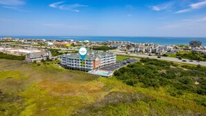 A coastal hotel with multiple buildings, a parking lot, and a view of the ocean. - La Dolce Vita II: Soundfront condo w/sunset views, community pool, 2 en-suites! (Nags Head)