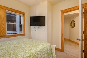 A bedroom with a bed, a TV mounted on the wall, a window, and a door leading to another room. - La Dolce Vita II: Soundfront condo w/sunset views, community pool, 2 en-suites! (Nags Head)