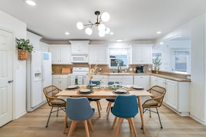 Una cocina moderna con armarios blancos, una mesa de comedor para cuatro personas y una araña.