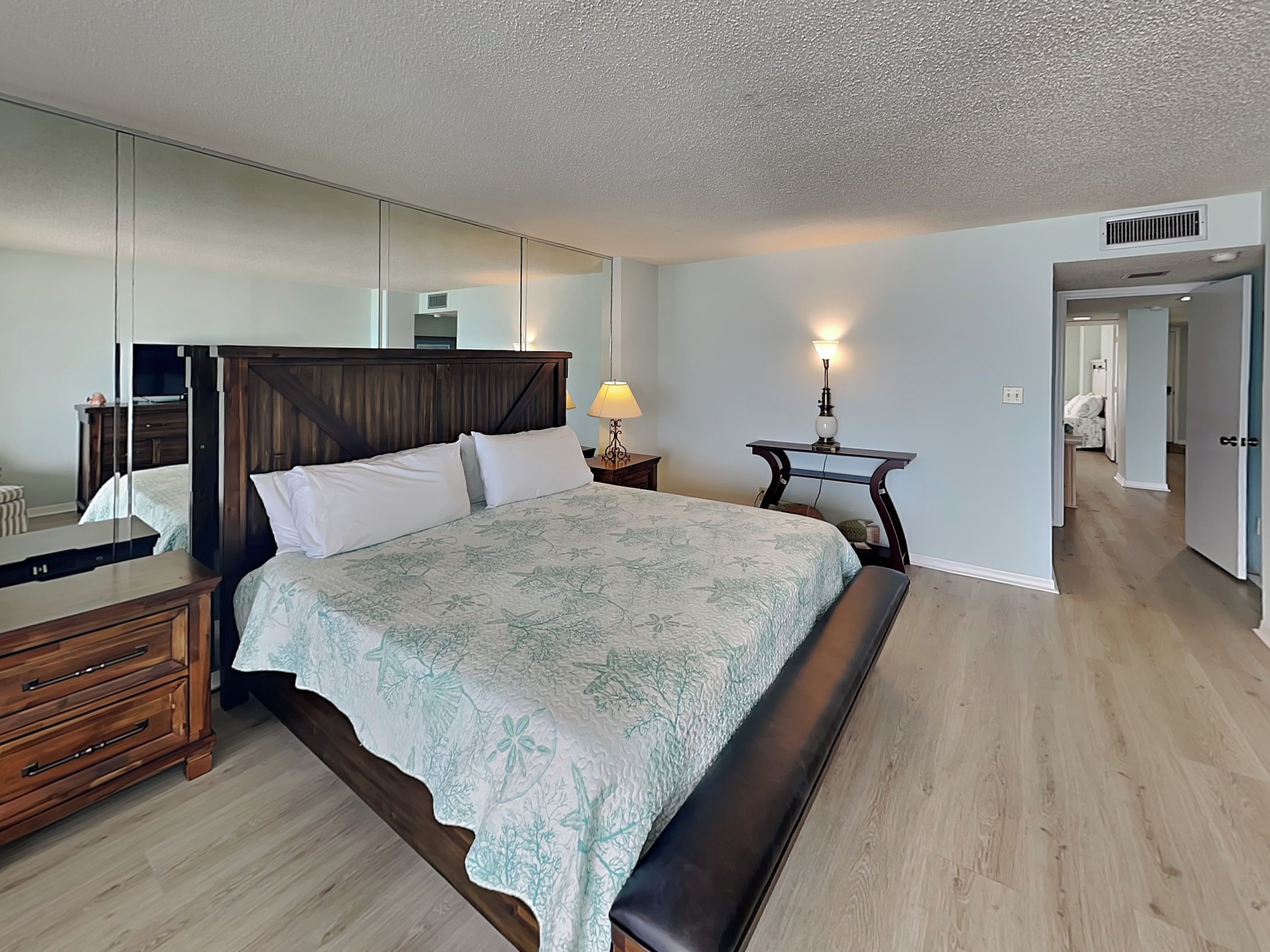 Un dormitorio con una cama grande, un aparador de madera, una mesita de noche con lámpara y un espejo en la pared.