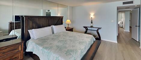 Un dormitorio con una cama grande, un aparador de madera, una mesita de noche con lámpara y un espejo en la pared.