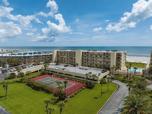 Un hotel con varios pisos, cancha de tenis y zona de piscina.
