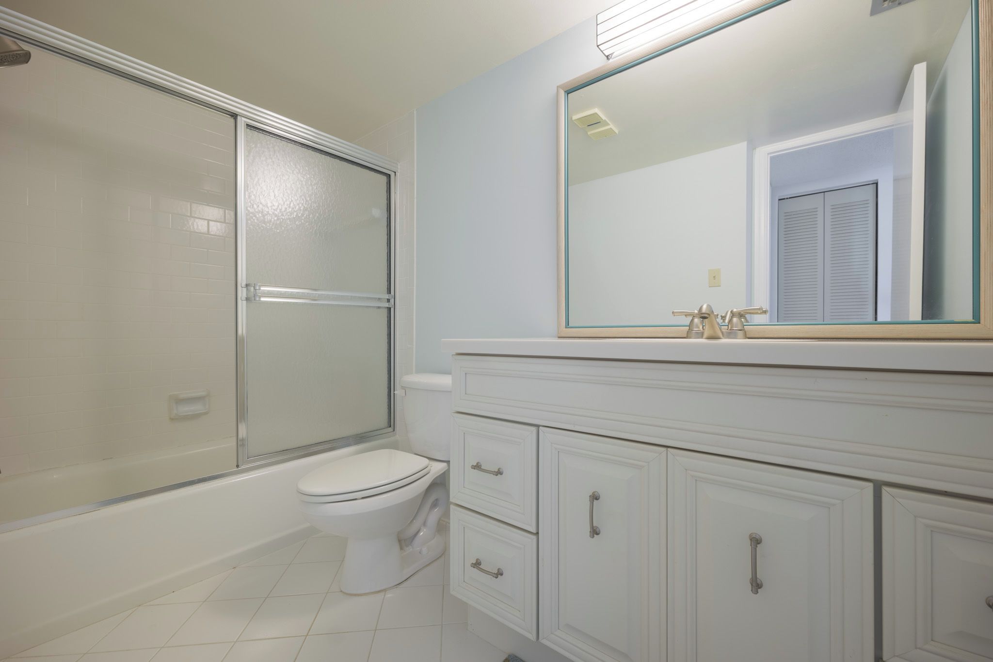 A bathroom with a glass-enclosed shower, a toilet, and a vanity with drawers and a mirror.