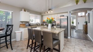 A modern kitchen with a central island, bar stools, a refrigerator, and a stove. - Casa De Mojave 3 Bedroom Home by RedAwning (Scottsdale)