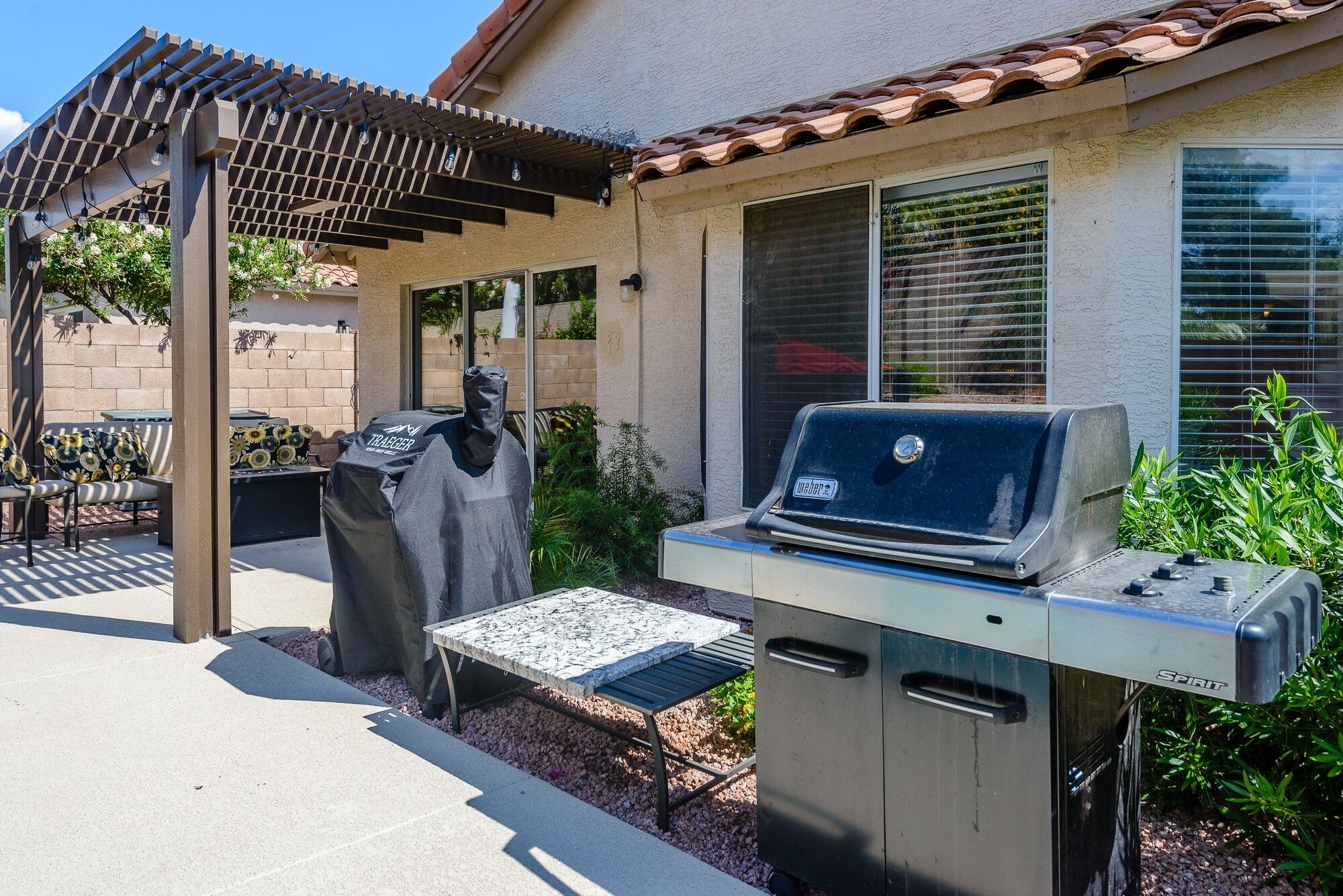 An outdoor patio with a grill, covered seating, and a pergola.