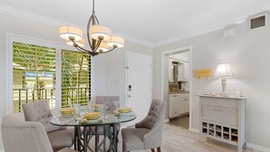 A dining area with a glass table, four upholstered chairs, and a chandelier. - Santa Maria II 110 by Distinctive Beach Rentals (Fort Myers Beach)