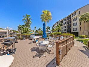 A deck with outdoor seating, a grill, and a view of a multi-story building with balconies. - Santa Maria II 110 by Distinctive Beach Rentals (Fort Myers Beach)