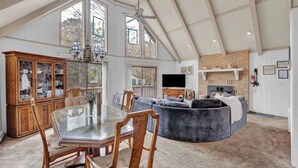 A spacious living area with a glass dining table, wooden chairs, a grey sofa, and a fireplace. - Poconos Retreat w/ Pool and Lake Access (Lake Ariel)