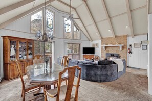 Un salón amplio con una mesa de comedor de cristal, sillas de madera, un sofá gris y una chimenea.