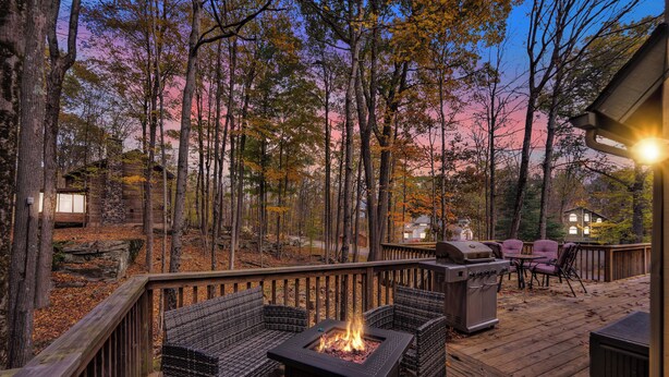 A deck with outdoor furniture, a fire pit, and a grill, surrounded by trees and a wooden deck. - Poconos Retreat w/ Pool and Lake Access (Lake Ariel)