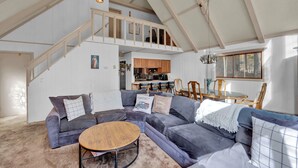 A spacious living area with a large gray sectional sofa, a round wooden coffee table, and a staircase leading to an upper level. - Poconos Retreat w/ Pool and Lake Access (Lake Ariel)