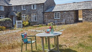 Une maison en pierre avec un jardin, une table ronde entourée de chaises et un portail blanc.