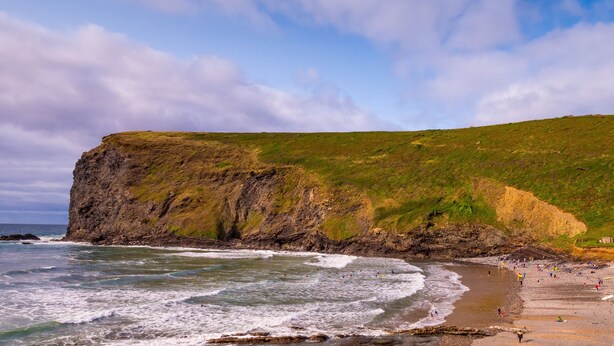 Un paysage côtier avec une falaise, une plage et des vagues de l’océan.