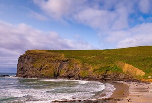 Un paysage côtier avec une falaise, une plage et des vagues de l’océan.