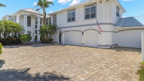 A two-story house with a white exterior, multiple garage doors, and a flag. - Dolce Vita Villa by Distinctive Beach Rentals (Cape Coral)