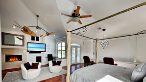A spacious bedroom with a large bed, two ceiling fans, a TV, a fireplace, and a view of the outdoors. - Dolce Vita Villa by Distinctive Beach Rentals (Cape Coral)