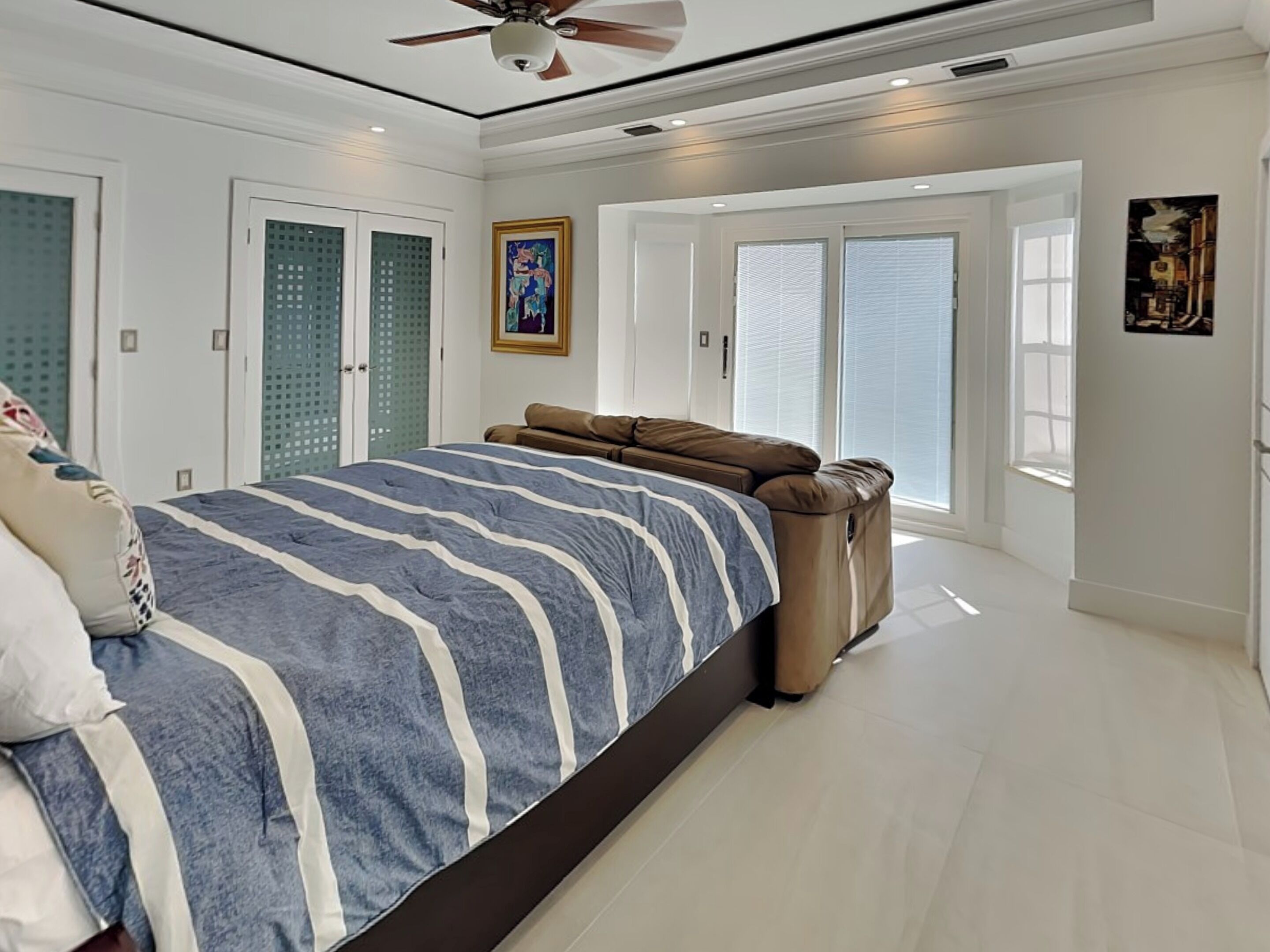 Ein Schlafzimmer mit einem großen Bett, einem Deckenventilator und einer Glastür, die auf einen Balkon führt.