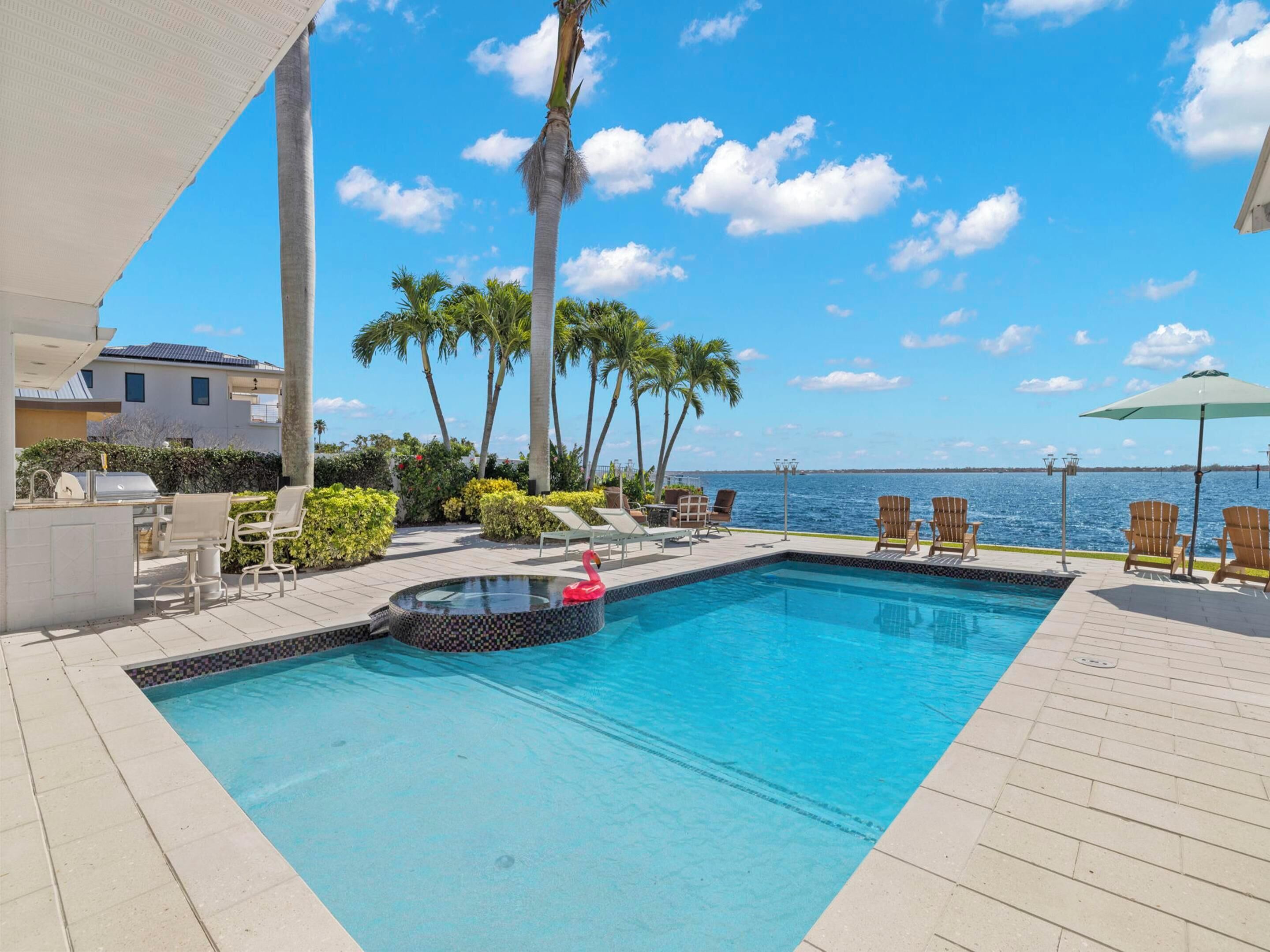 A swimming pool with lounge chairs, a flamingo float, and a view of the ocean.