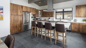 A modern kitchen with wooden cabinets, a stainless steel refrigerator, a central island with bar stools, and a large window. - Rendezvous Game Trail | Luxe Mountain Home | Brand New Build | Amazing Views (Fraser)
