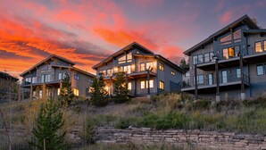 A modern multi-story residential building with large windows and balconies, set against a sunset sky. - Rendezvous Game Trail | Luxe Mountain Home | Brand New Build | Amazing Views (Fraser)