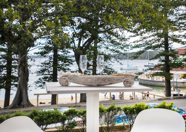 A table with a decorative object and two glasses, overlooking a waterfront with people and boats.