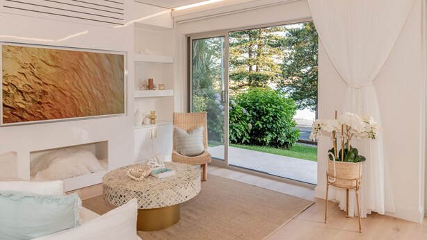 Un salon moderne avec un grand tableau, une table basse ronde, un fauteuil en osier et une vue sur la verdure à l’extérieur.