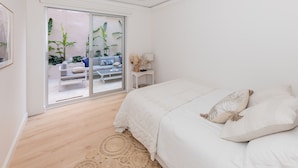 Une chambre avec un grand lit, une porte-fenêtre coulissante donnant sur un balcon agrémenté de plantes et un canapé bleu.