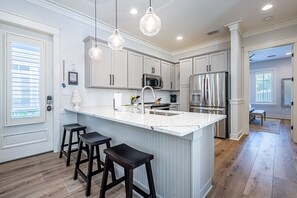 Una cocina moderna con muebles blancos, una isla grande con taburetes de bar, electrodomésticos de acero inoxidable e iluminación colgante.