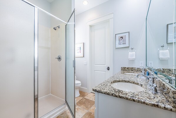 A bathroom with a glass shower enclosure, a granite countertop sink, and a white toilet.